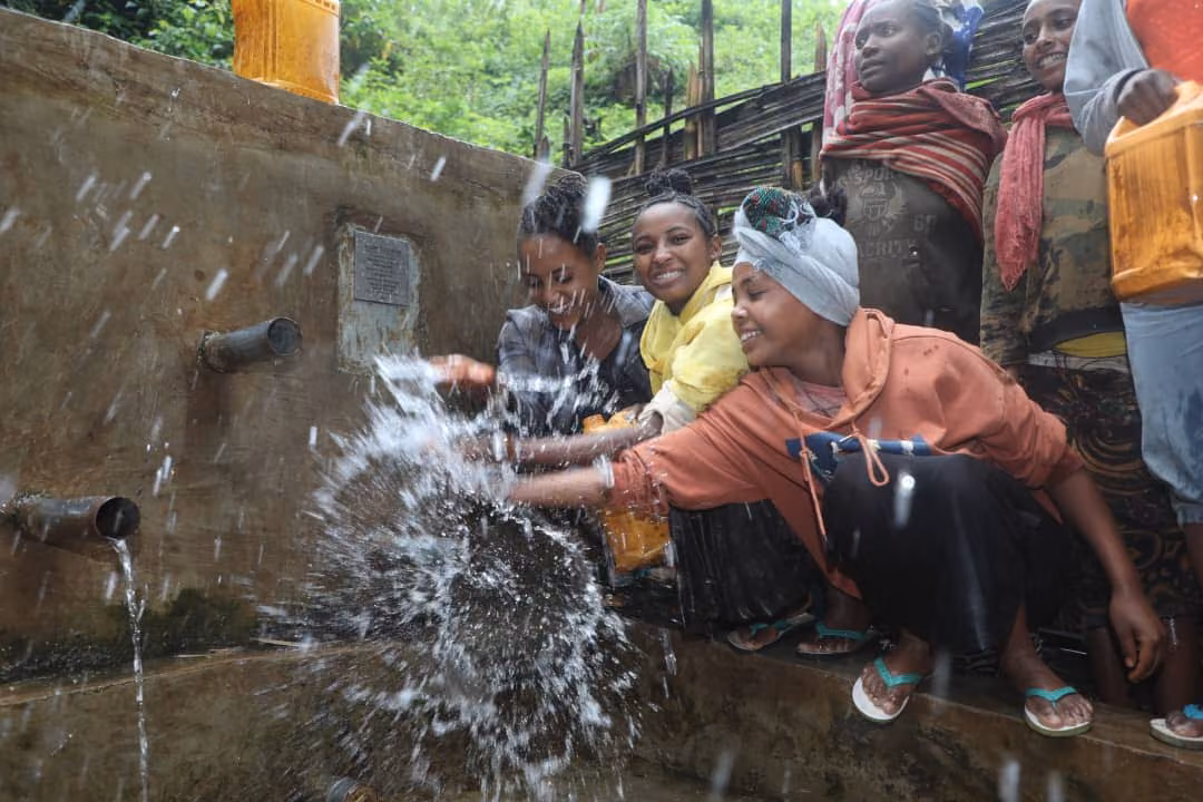 Young women joyfully splashing water at the Gogolano well in Sidama, Ethiopia